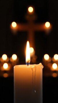 Burning candle with soft light and cross in dark background