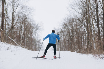 Man cross-country skiing uphill through winter forest