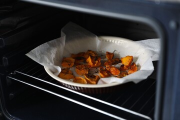 Baking dish with pieces of pumpkin and thyme in oven, closeup