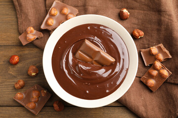 Melted chocolate and pieces with hazelnuts on wooden table, flat lay