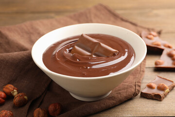 Melted chocolate and pieces with hazelnuts on wooden table, closeup