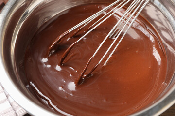 Melted chocolate and whisk in bowl on table, closeup