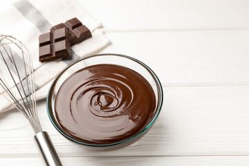 Melted chocolate, whisk and pieces white on wooden table, closeup. Space for text