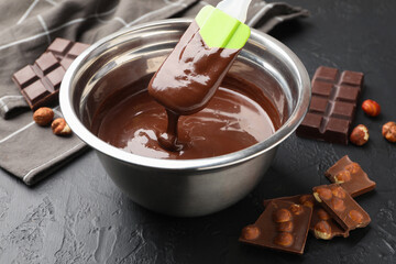 Melted chocolate and pieces with hazelnuts on black table, closeup