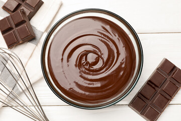 Melted chocolate, whisk and pieces white on wooden table, flat lay