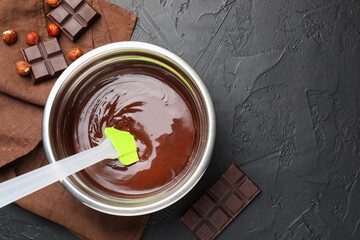 Melted chocolate and pieces with hazelnuts on black table, flat lay. Space for text
