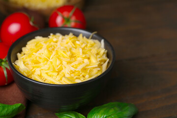 Grated cheese in bowl, tomatoes and basil on wooden table, closeup. Space for text