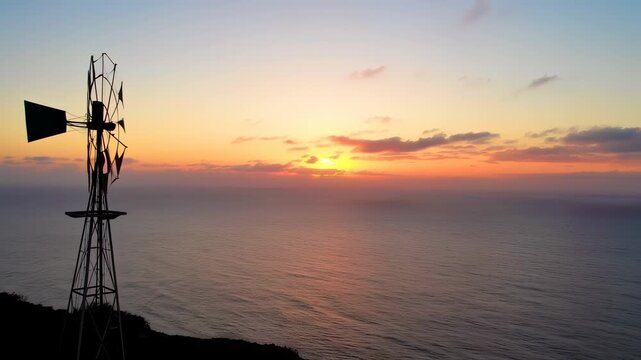A silhouette of a windmill against a vibrant sunset over calm ocean water