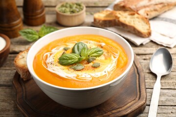 Delicious pumpkin cream soup with basil and seeds served on wooden table, closeup