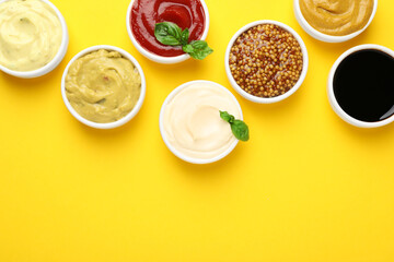 Different sauces and herbs on yellow background, flat lay. Space for text