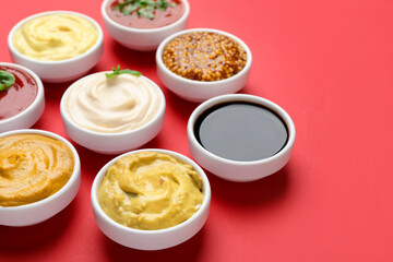 Different sauces in bowls on red background, closeup