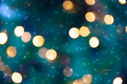 Golden bokeh lights on a dark background. Snowflakes falling down. Christmas magical light background, overlay or lens flare effect