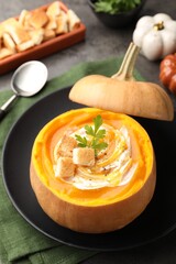Tasty pumpkin cream soup with croutons and parsley served in pumpkin on table, closeup