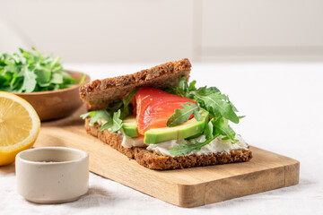 Open sandwich on whole grain bread with smoked salmon, soft cheese, avocado and arugula, healthy gourmet breakfast