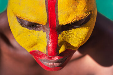 portrait single young african woman smiling; tribal yellow face paint; headshot close-up