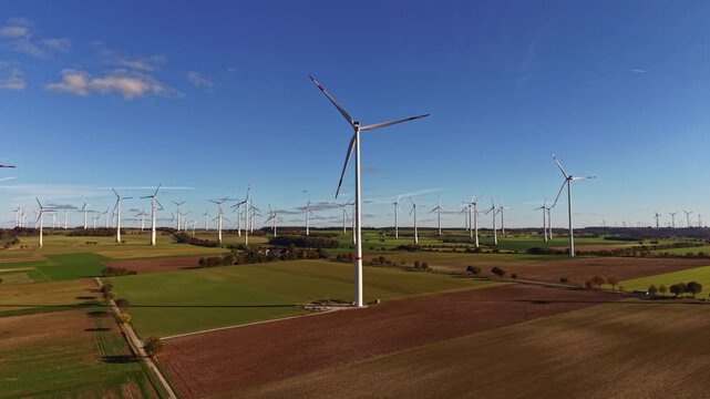 Rows of tall wind turbines stretch across the green fields harnessing wind energy on a bright day The landscape is peaceful showcasing technology and nature side by side