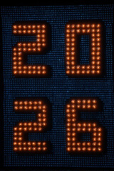 celebrate 2026 with glowing marquee light bulbs in warm color on dark blue digital led background, club new years eve, silvester, portrait format, photorealistic