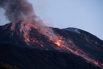 Powerful night eruption with flowing lava, sparks, and heavy smoke from the crater of Stromboli volcano, Sicily, Italy.