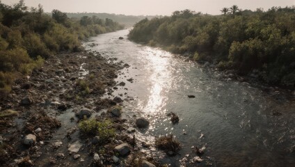 Serene River Flowing Through Lush Greenery and Rocky Banks Under a Hazy Sky.