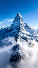The majestic Matterhorn mountain peak covered in snow rises above the clouds against a clear blue sky.