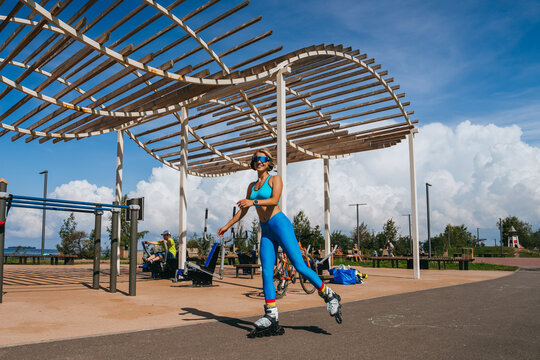 Woman roller-skating dynamically under a modern pergola, exuding energy and style in vivid sporty clothes.