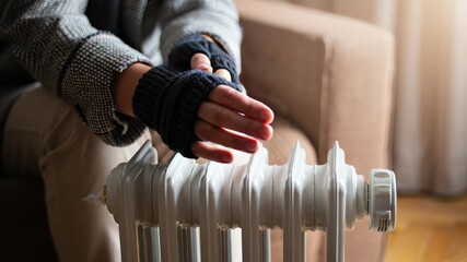 Person warming hands with fingerless gloves on home radiator during winter.
