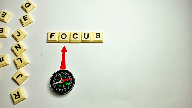 Creative minimalist concept showing the word FOCUS with a compass pointing upward, surrounded by scattered letters, symbolizing direction,clarity, concentration,and finding purpose amidst distraction.