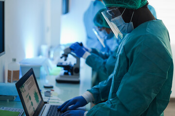 Medical workers in hazmat suit working with microscope inside laboratory hospital wearing safety masks - Healthcare, longevity and medical research concept - Focus on african man face