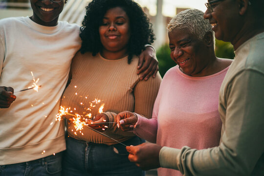 Happy african family celebrating with sparklers during new year's eve - Father, mother, daughter and son having fun together during winter holidays - Main focus on mum face