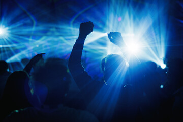Silhouettes dancing under blue laser lights at concert