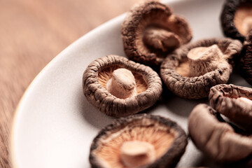 Edible dehydrated shiitake mushrooms in dish on wooden kitchen counter. Nutritious ingredient