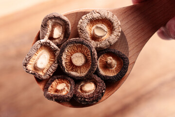 Dried organic shiitake mushrooms in a wooden spoon held by a hand. Top view