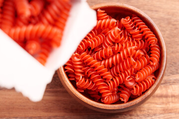 Red lentil pasta is poured into wooden bowl from white paper package