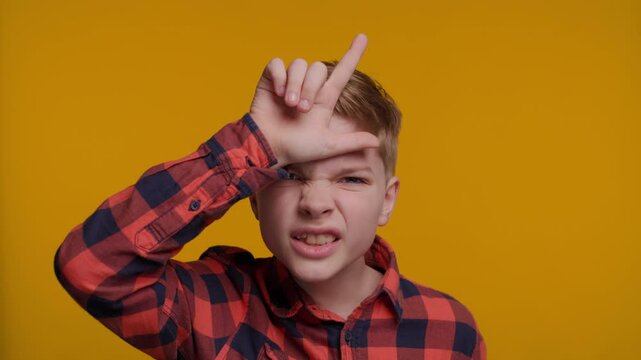 Boy Showing Letter L on Forehead with Hands Saying 'Loser' on Yellow Background