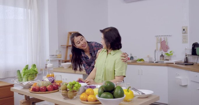 Senior asian mother and adult daughter smiling warmly in kitchen, preparing salad with colorful fruit and vegetable, teamwork and happiness showing family bonding, healthy lifestyle, love, wellbeing