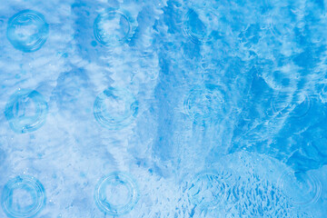 Blue ice background. Blue water with ripples on the surface. Defocus blurred transparent blue colored clear calm water surface texture with splashes and bubbles. Water waves with shining pattern.