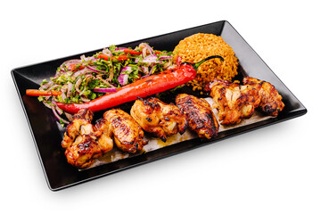 Grilled chicken skewers served with rice and salad on a black plate