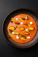 Mussels in tomato sauce garnished with herbs and greens on a dark plate
