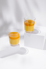 Bright tropical dessert glasses filled with creamy mango mousse and vibrant passion fruit sauce under soft studio lighting on white geometric blocks