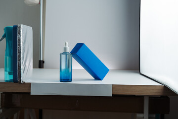Behind-the-scenes view of product photography setup with softbox, white background, and reflector propped on a spray bottle, mobile photo. Concept of studio, lighting, photography, setup.
