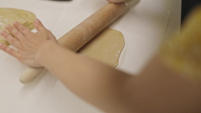 Woman's hands rolling dough with a wooden pin