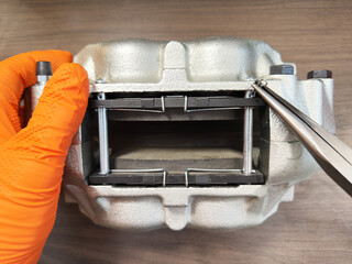 Closeup of a new silver brake caliper and pads being prepared in a workshop to fit onto a vehicle,...