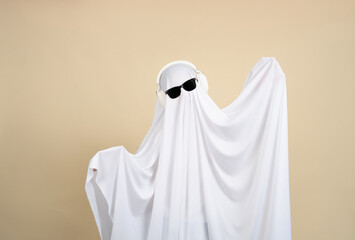 Cool ghost, person in ghost costume wearing headphones dancing happily on beige background.