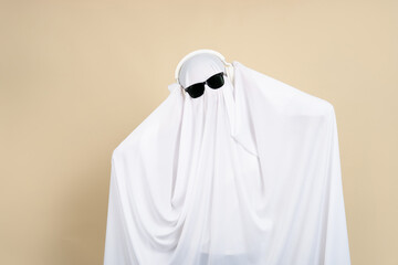 Woman in a white ghost costume is listening to her favorite music with headphones on a beige background.