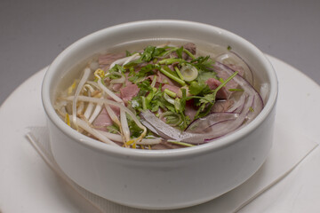 A bowl of ph, a Vietnamese noodle soup, with herbs and meat toppings