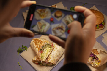 A person is taking photographs of a variety of food items beautifully arranged on a table with a smartphone