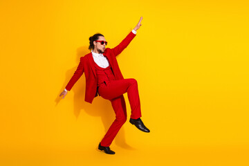 Funny red suited man leaps with energy in bright yellow studio creating bold stylish vibe for fashion and entertainment shoot