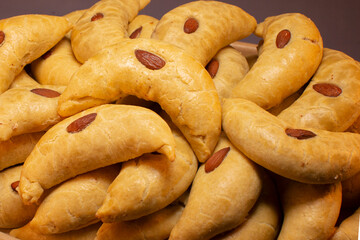 Rustic cookies with nut filling, Homemade flaky cookies with almond garnishes, Cozy seasonal dessert featuring almondtopped flaky pastries on wooden serving