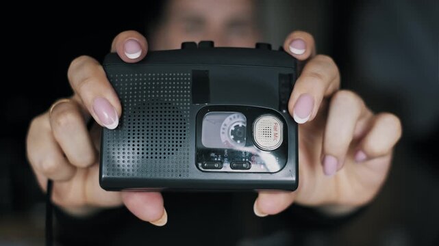 Closeup of female hands with manicure holding a retro style audio player. A portable cassette tape spins inside the old 90s device, a popular 2000s fashion accessory.