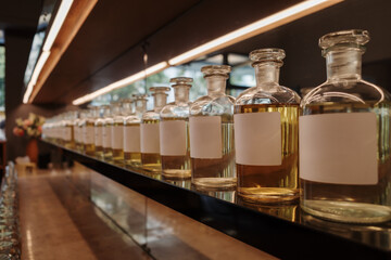 A low-angle, perspective shot of a long row of glass apothecary bottles filled with yellow perfume...